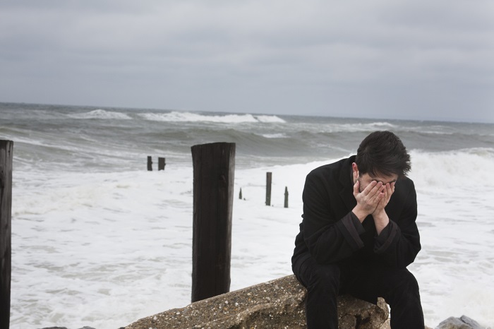 a sad man crying near the ocean